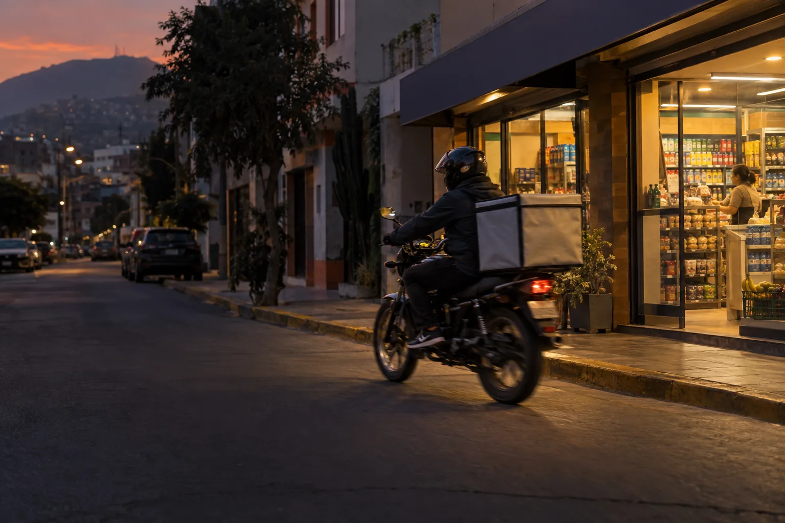 Un repartidor en moto sale con un pedido desde una tienda de barrio iluminada al anochecer